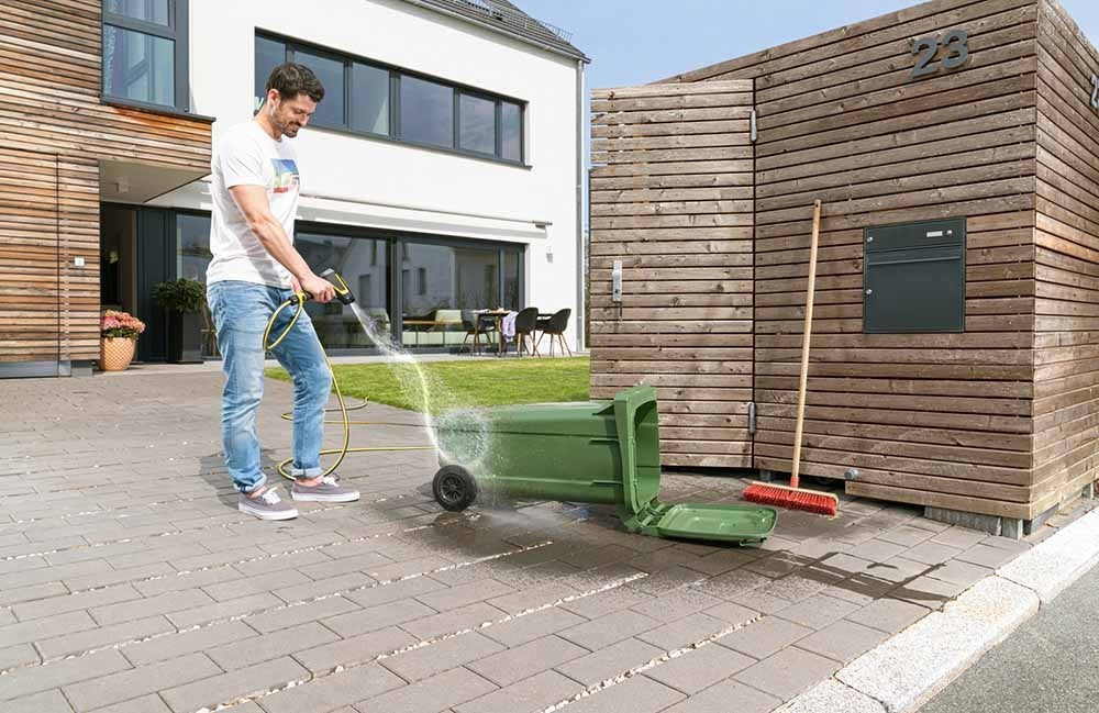 Mann reinigt grünen Müllbehälter mit Kärcher WBS 3 Reinigungspistole und Rotationsstrahl